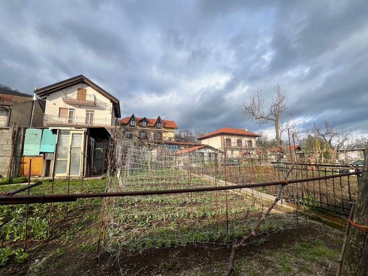 Rural hillside village with vegetable gardens and houses beneath dramatic cloudy skies.