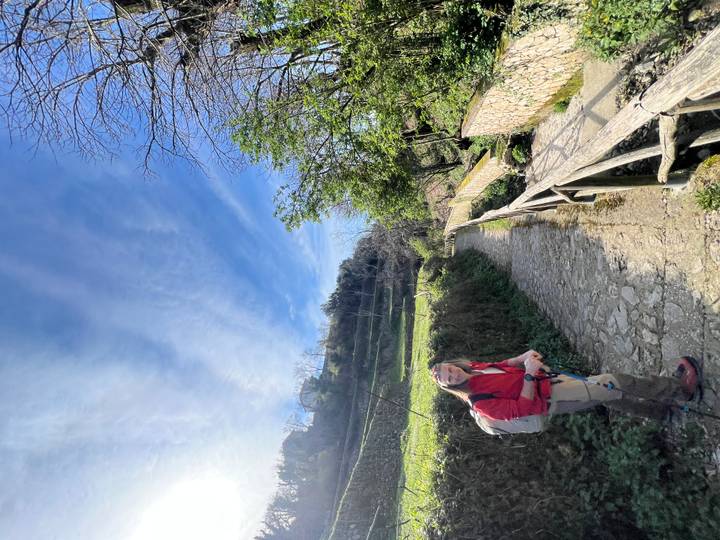 Female hiker on a stone path bordered by terraces and greenery under a blue sky.