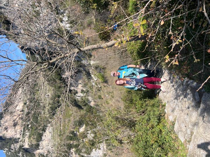 Two hikers on a rocky mountain trail surrounded by steep green cliffs.