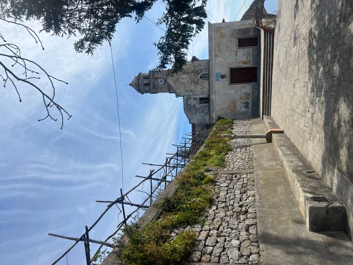 Stone church with clock tower in a small Italian hill town beneath streaked clouds.