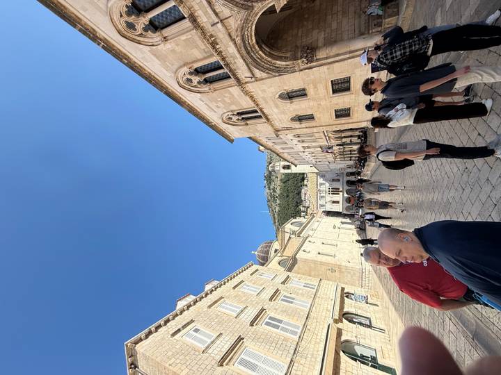 Busy pedestrian street in Dubrovnik’s Old Town with historic limestone facades under a bright blue sky.