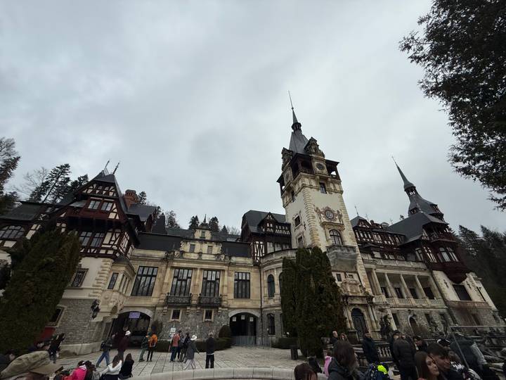 Neo-Renaissance Peles Castle surrounded by evergreen trees under a cloudy sky in Romania.