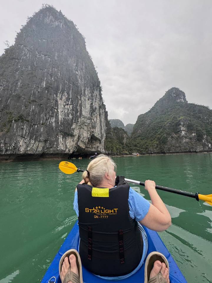 Kayaker paddling emerald waters beneath towering limestone cliffs of Ha Long Bay.