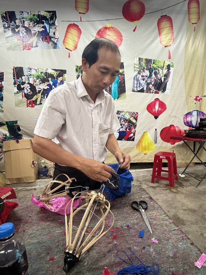 Craftsman preparing materials in a lantern workshop decorated with hanging silk lanterns.