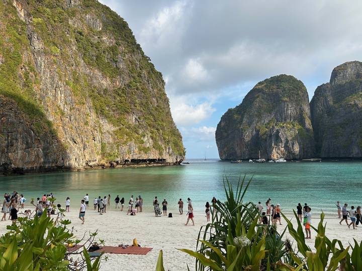 Crowds enjoy turquoise waters and white sand surrounded by towering limestone cliffs at a famous Thai bay.