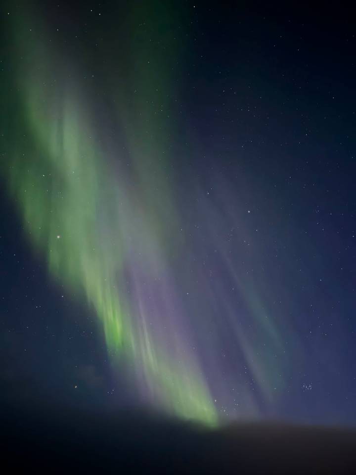 Vibrant green and purple northern lights sweeping across a star-filled night sky.