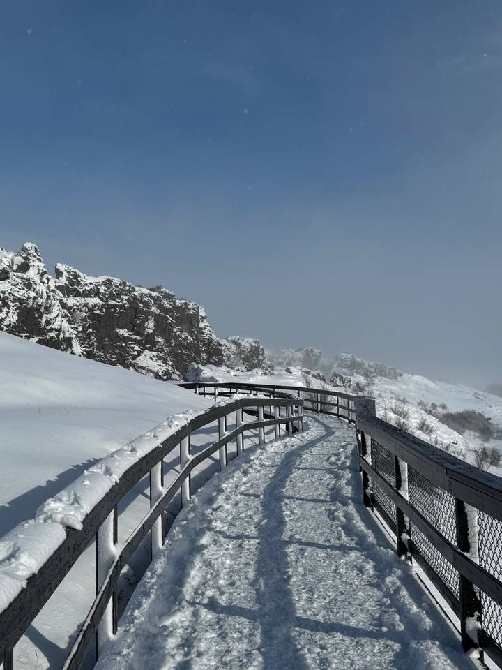 Snow-covered boardwalk curving alongside rugged cliffs under clear blue sky in a national park.