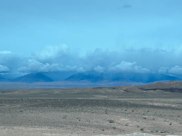 Wide arid plain with distant mountains beneath a bank of dramatic clouds.