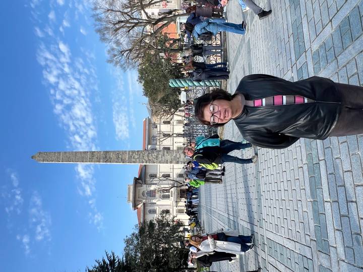 A woman stands smiling in front of an ancient obelisk on a sunny square.