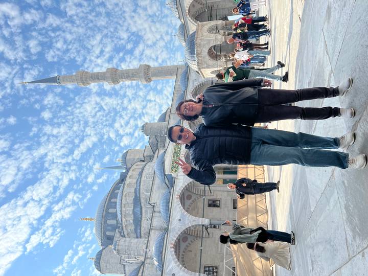 A smiling couple poses in front of the grand domes and minarets of a mosque.