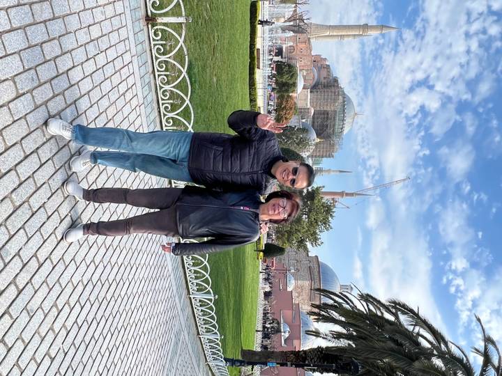 A couple gestures happily with Hagia Sophia and cranes visible in the background.