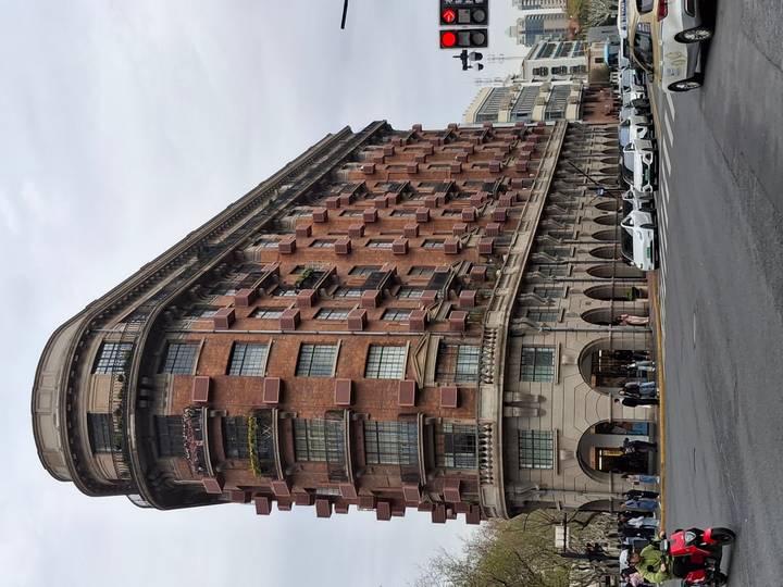 Historic red-brick Normandie apartment building (Wukang Mansion) on a gray day with traffic and pedestrians below.
