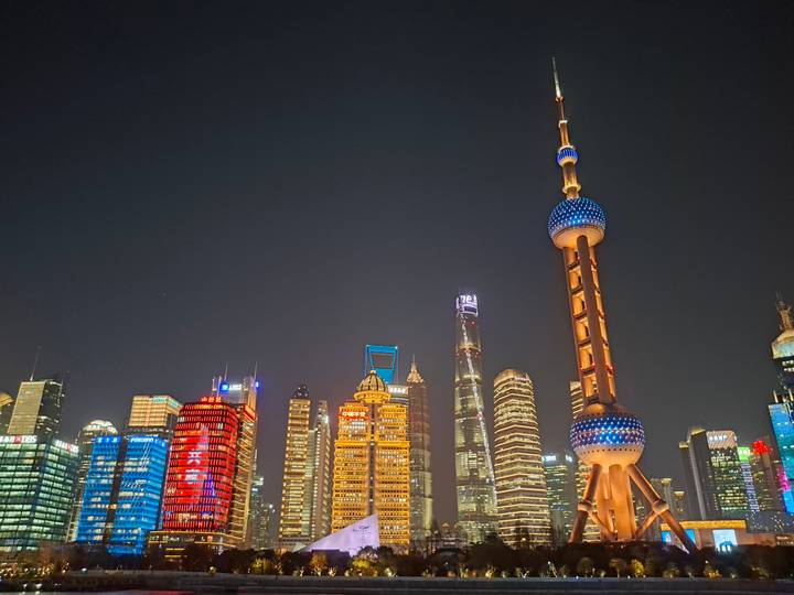 Night view of Shanghai’s Pudong skyline with the brightly lit Oriental Pearl Tower and surrounding skyscrapers against a clear sky.