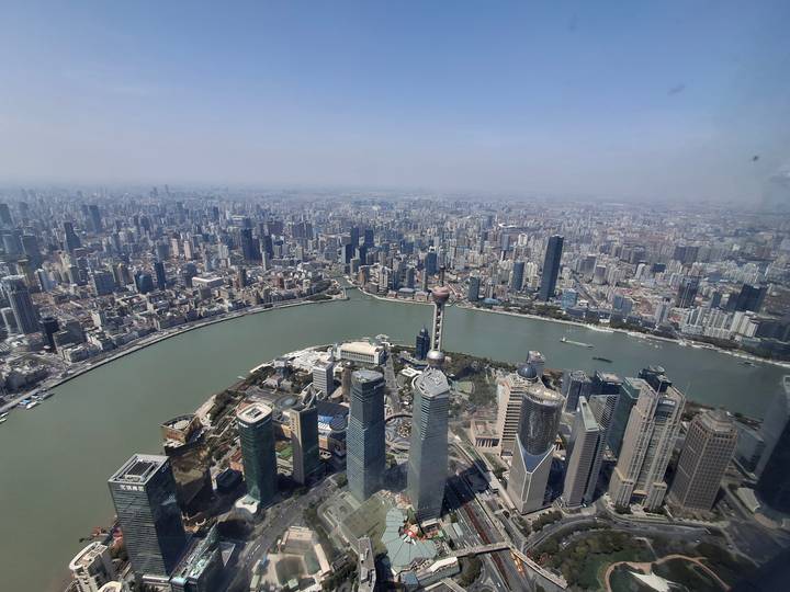 High-altitude daytime panorama of Shanghai overlooking the Huangpu River, Oriental Pearl Tower and countless skyscrapers stretching to the horizon.