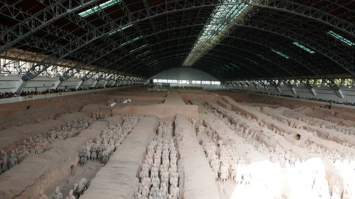Wide interior shot of the main pit of the Terracotta Army in Xi’an, rows of clay warriors under a vast arched hangar roof with visitors along the sides.