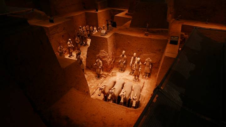 Close-up view into a sunken excavation of Terracotta Warriors lit by warm spotlights, revealing detailed figures and horses.