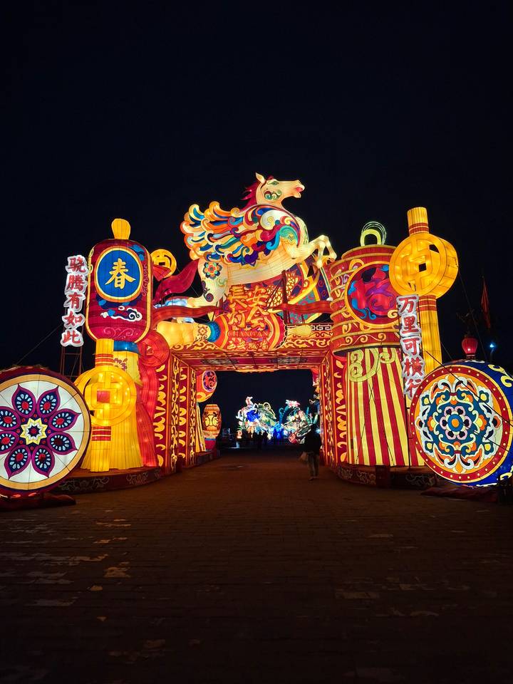 Colorful illuminated lantern gate festooned with traditional Chinese motifs and characters during a night festival.