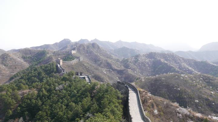 Expansive daylight view of the Great Wall of China snaking across rugged, forested mountain ridges.