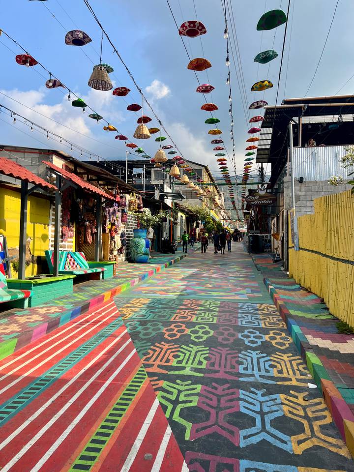 Vibrant pedestrian street with multicoloured painted pavement, hanging umbrellas and handicraft shops in a Guatemalan lakeside town.