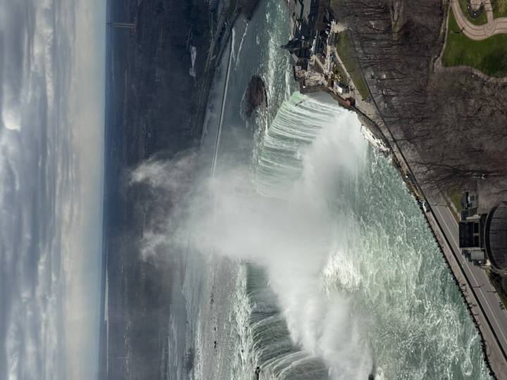 Aerial view of Horseshoe Falls at Niagara with powerful mist plume rising into a cloudy sky.