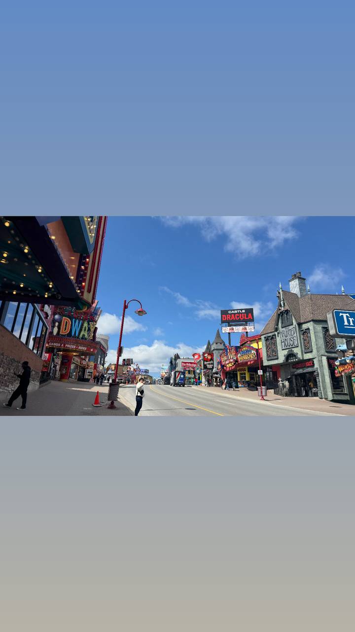 Colourful Clifton Hill entertainment strip in Niagara Falls lined with neon signs and themed attractions on a bright day.
