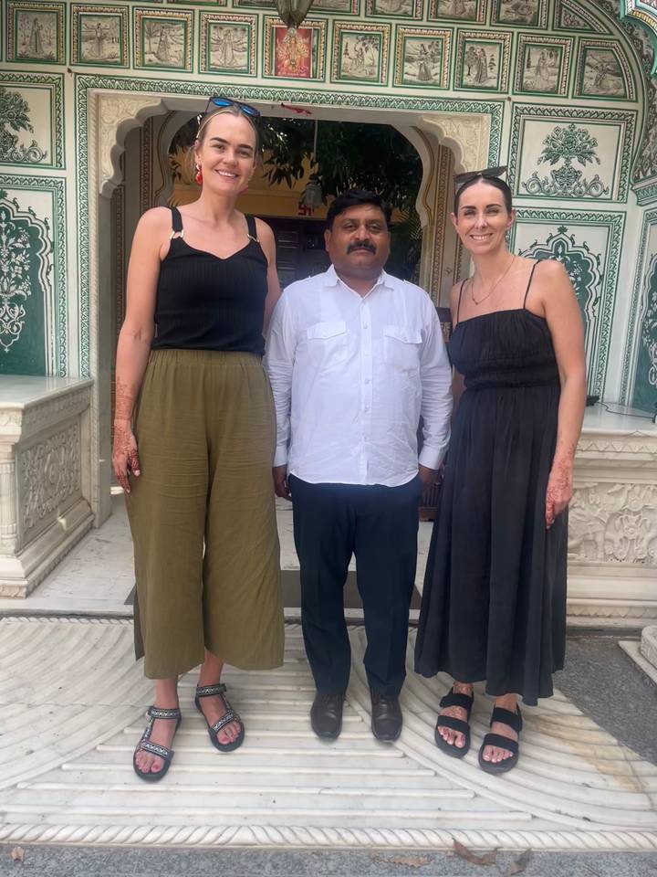 Three travelers pose with a local guide in front of ornate marble carvings at an Indian temple entrance.