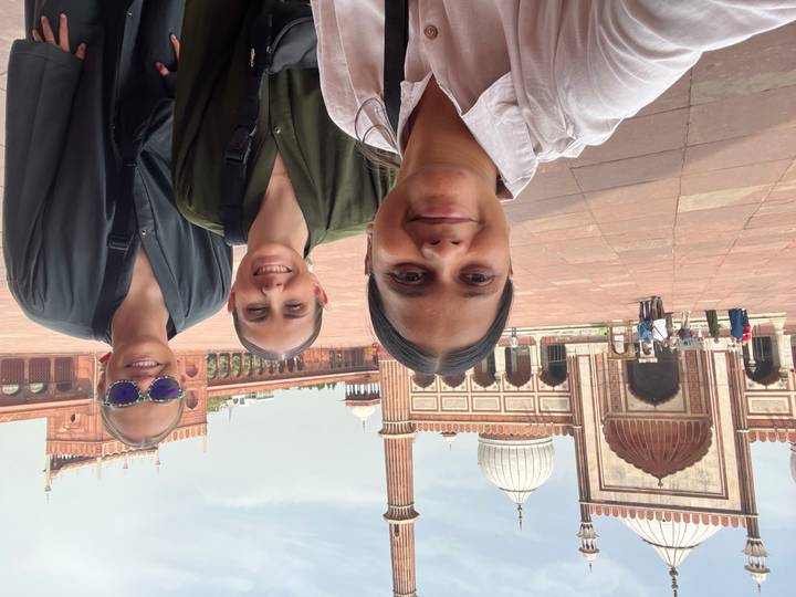 Selfie of three friends in courtyard of Jama Masjid with its grand gateways and domes behind.
