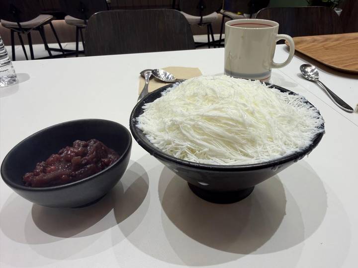 Korean shaved-ice dessert (bingsu) piled high beside a bowl of sweet red bean paste on a table.