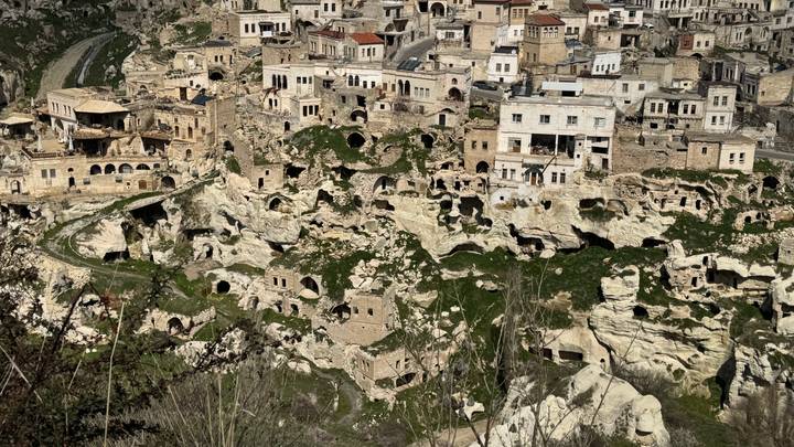 Historic hillside town with cave houses and stone buildings carved into white cliffs.