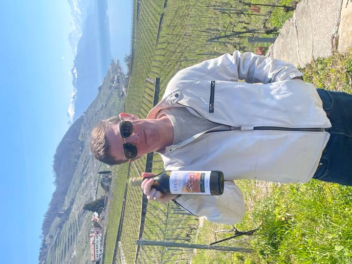 Traveler in sunglasses holding a bottle of Swiss wine in terraced vineyard overlooking Lake Geneva and Alps