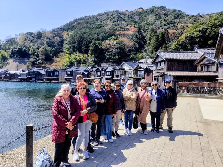 Tourists standing beside traditional waterside boathouses in coastal Japanese village