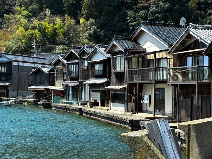 Row of traditional wooden boathouses lining calm blue water in rural Japan