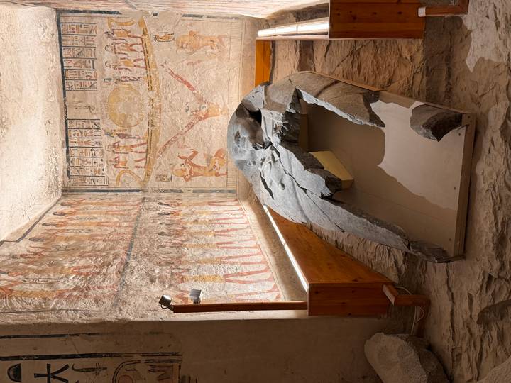 Fragmented granite sarcophagus inside vividly painted Egyptian tomb chamber