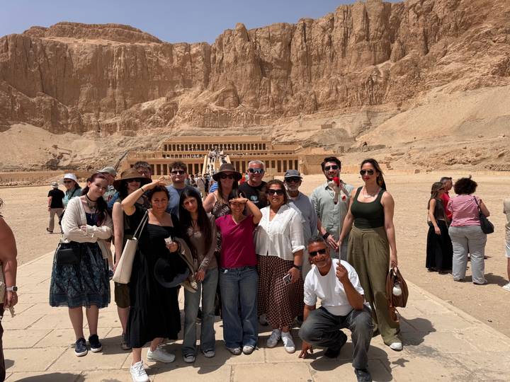 Tour group posing in front of Hatshepsut Temple against towering cliffs