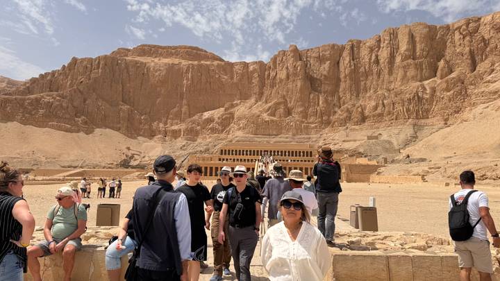 Tourists walking toward Hatshepsut Temple beneath desert cliffs