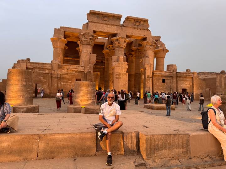 Tourists gather in front of a lit sandstone temple with massive columns at dusk