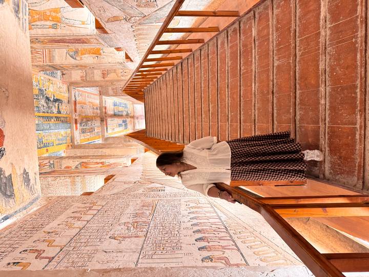 Woman looks up at colourful hieroglyphic walls while standing on a terracotta staircase inside a tomb