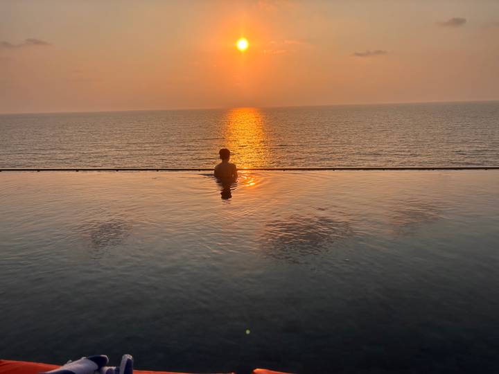 Silhouette of a person in an infinity pool watching the sun set over the ocean horizon