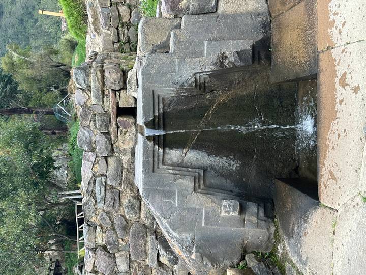 An ancient stone fountain pours clear water through an Inca-style carved channel.