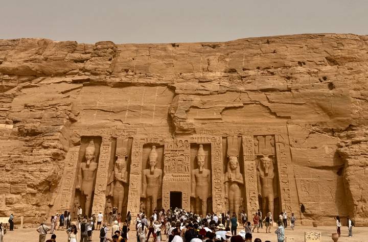 Grand rock-cut façade of Abu Simbel temple with crowds gathered at its base.
