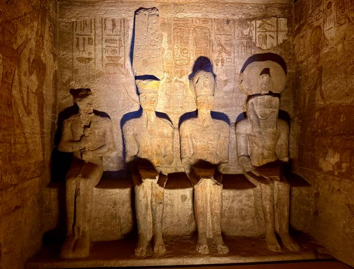 Dimly lit interior shows four seated sandstone statues carved into a temple wall.