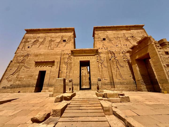 Twin pylons of a sandstone temple adorned with large reliefs under harsh desert sun.