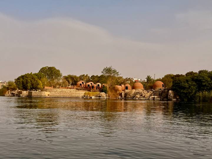 Small island on the Nile dotted with domed brick buildings and lush trees at sunset light.