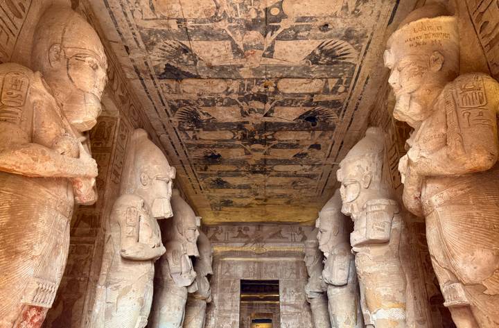 Hallway lined with colossal statues and intricate painted ceiling inside Abu Simbel.