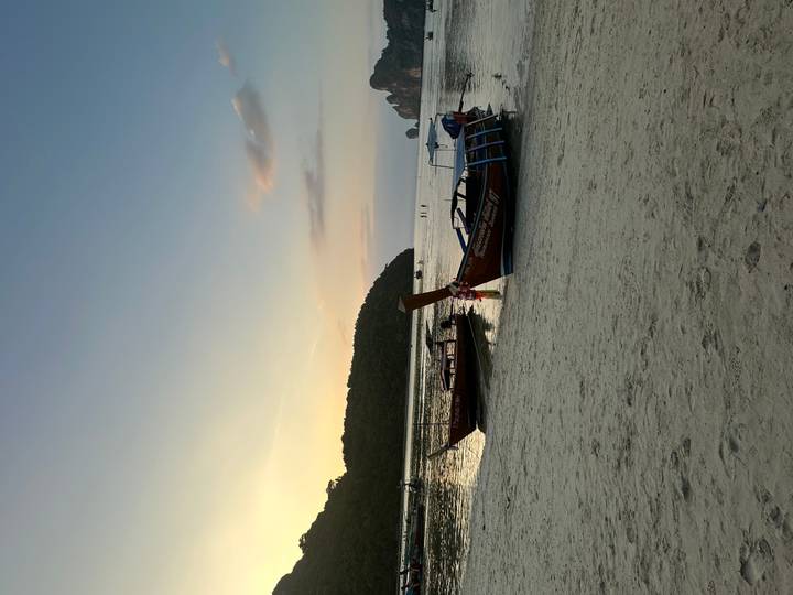 Traditional long-tail boats rest on sandy shore at dusk with forested hills beyond.