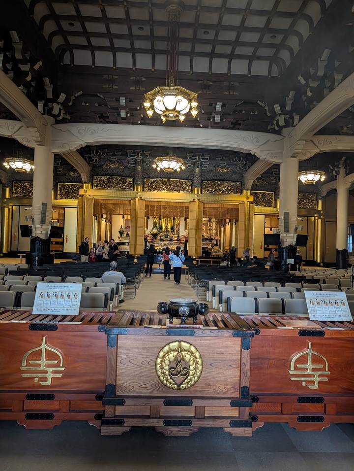 Interior of a large Buddhist hall with visitors seated before an ornate altar