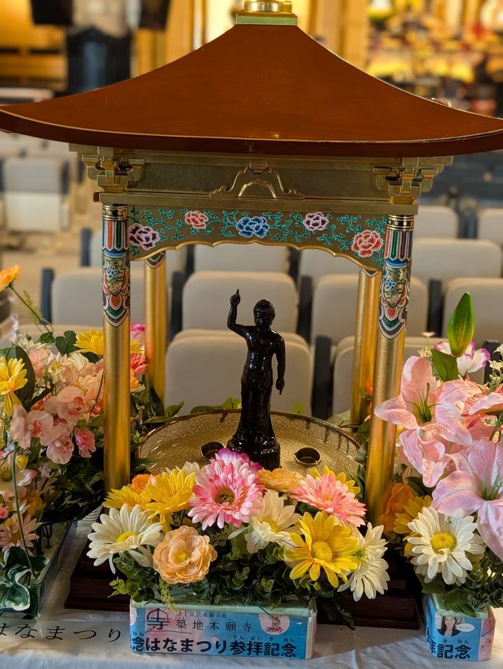 Black Buddha infant statue under a floral canopy inside a temple hall