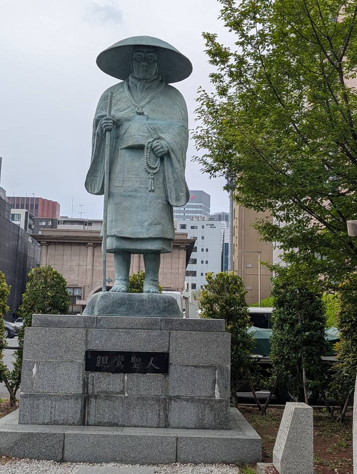 Partial bronze statue of a robed figure with city buildings in the background