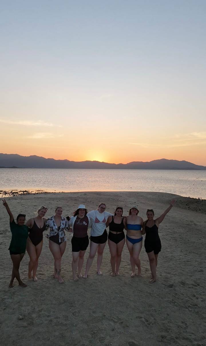 Group of travelers silhouetted against a pastel sunset on a tropical beach.