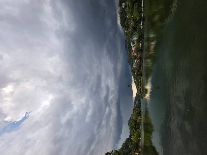 Calm lake reflecting dramatic dark storm clouds with townscape and greenery beyond.